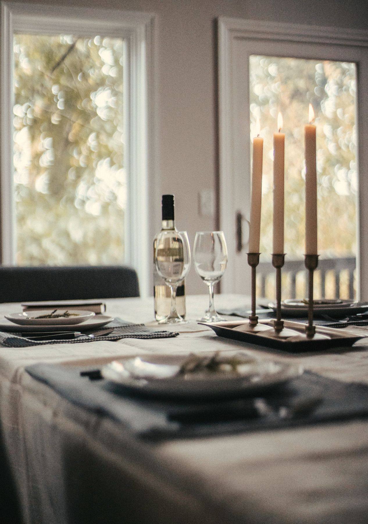 A table set by a window with candles and a bottle of white wine